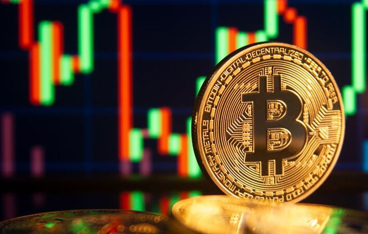 una moneta di Bitcoin con un grafico sull'andamento di prezzo sullo sfondo