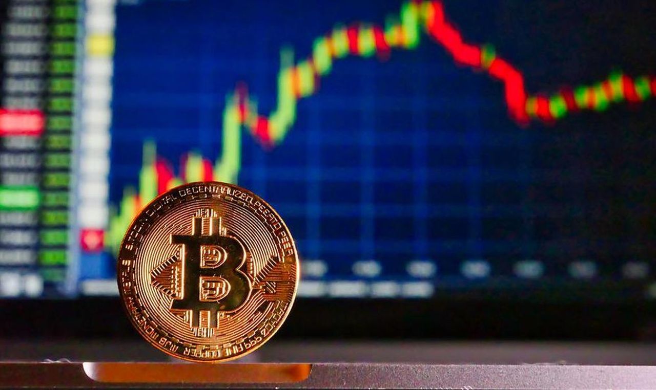 una moneta di Bitcoin con un grafico sull'andamento di prezzo sullo sfondo