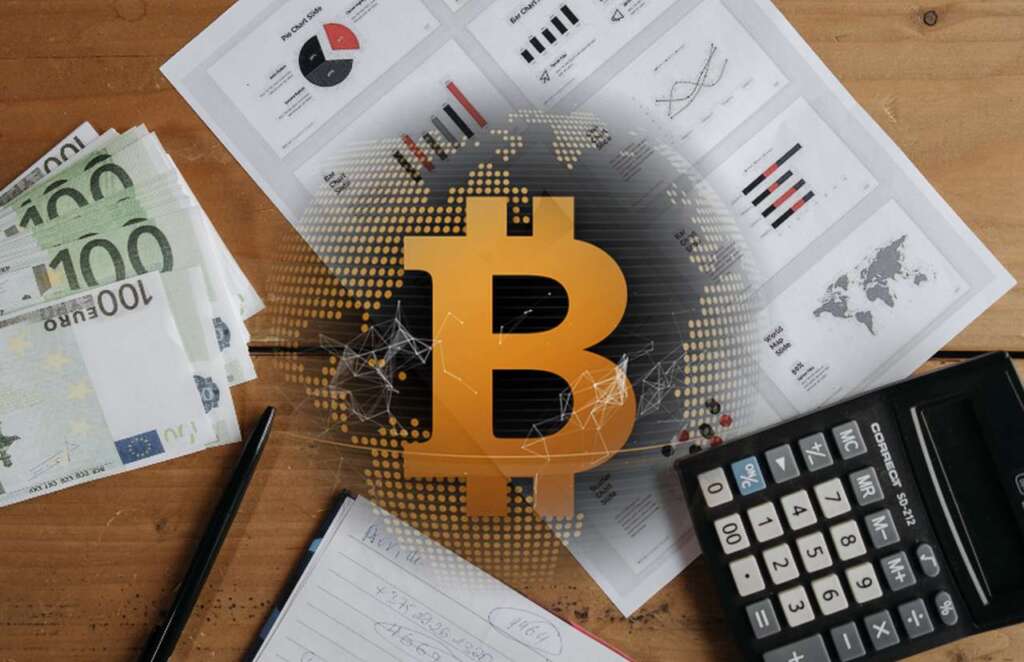 una calcolatrice, delle banconote da 100 euro e alcuni documenti con grafici su un piano di legno, con il logo di Bitcoin in sovrimpressione