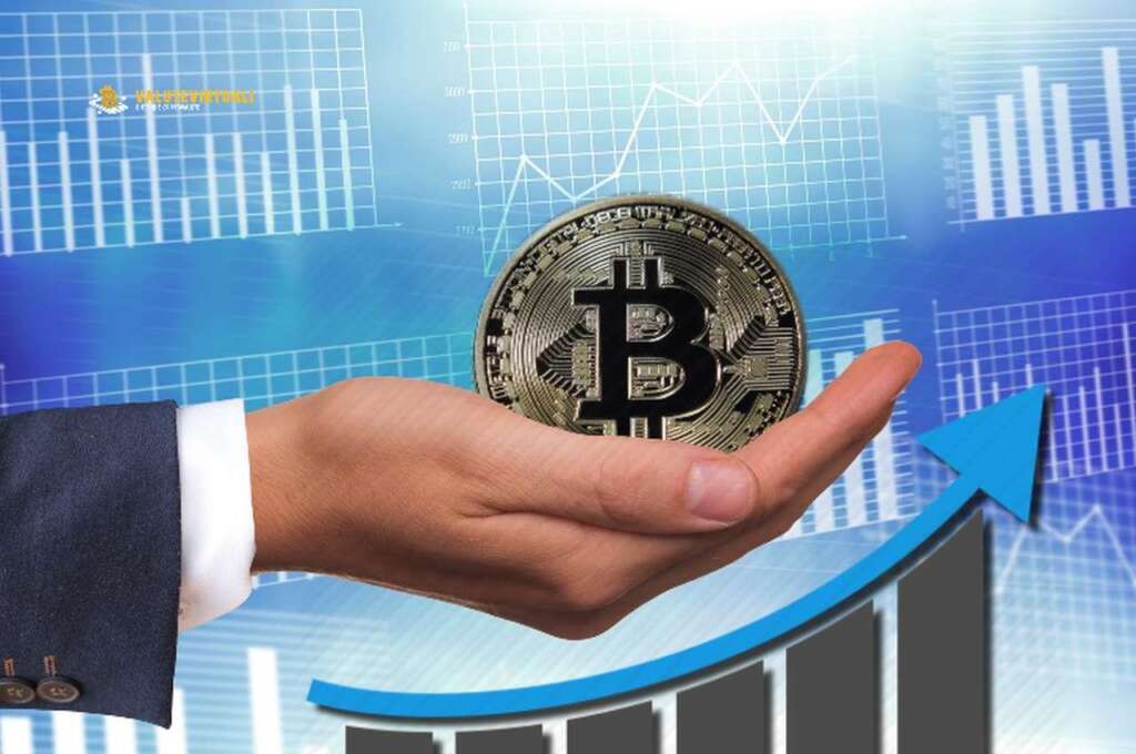 Una moneta di Bitcoin nel palmo di una mano, e sotto di essa un grafico con una freccia