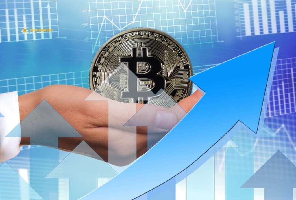 una moneta di Bitcoin di grosse dimensioni nel palmo di una mano. In sovrimpressione in trasparenza diverse frecce verso l'alto