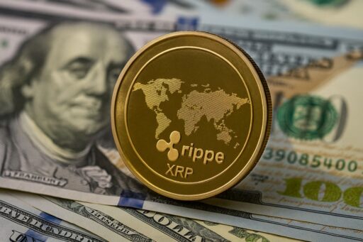 Una moneta con in piccolo il simbolo di XRP e una mappa del mondo. Sullo sfondo delle banconote